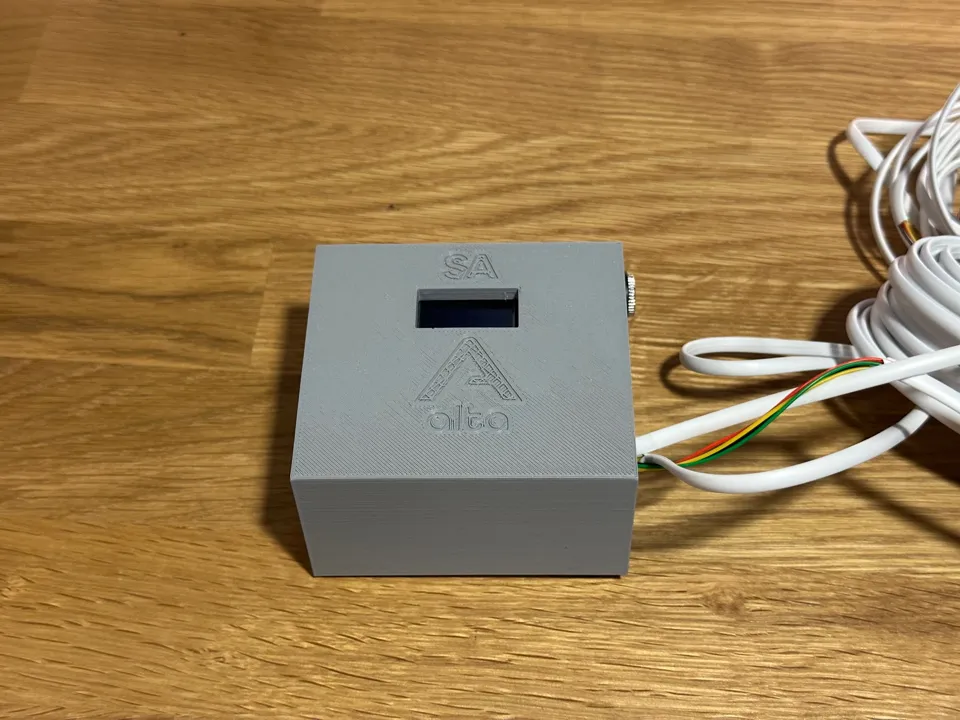 The Alta sensor, a small 3D-printed gray box with a display window, on a wooden table.